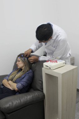 Esmer tenli Latin doktor, epilepsi teşhisi koymak için 30 yaşındaki bir kadının elektroensefalogram EEG 'si için telleri kafaya bağlıyor.