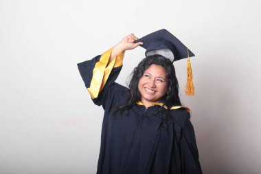 Mezuniyetini kutlamak için kep ve cübbe giyen 25 yaşında genç esmer bir kadın. Gururlu, memnun ve mutlu bir şekilde okulu bitirmiş.