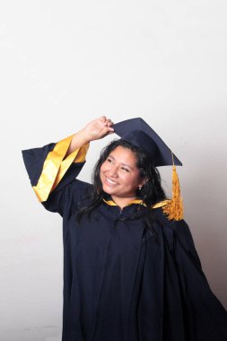 Mezuniyetini kutlamak için kep ve cübbe giyen 25 yaşında genç esmer bir kadın. Gururlu, memnun ve mutlu bir şekilde okulu bitirmiş.