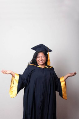 Mezuniyetini kutlamak için kep ve cübbe giyen 25 yaşında genç esmer bir kadın. Gururlu, memnun ve mutlu bir şekilde okulu bitirmiş.