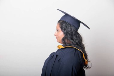 Mezuniyetini kutlamak için kep ve cübbe giyen 25 yaşında genç esmer bir kadın. Gururlu, memnun ve mutlu bir şekilde okulu bitirmiş.