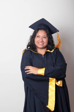 Mezuniyetini kutlamak için kep ve cübbe giyen 25 yaşında genç esmer bir kadın. Gururlu, memnun ve mutlu bir şekilde okulu bitirmiş.