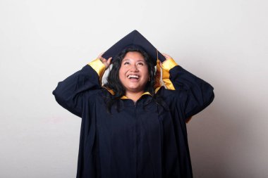 Mezuniyetini kutlamak için kep ve cübbe giyen 25 yaşında genç esmer bir kadın. Gururlu, memnun ve mutlu bir şekilde okulu bitirmiş.