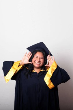 Mezuniyetini kutlamak için kep ve cübbe giyen 25 yaşında genç esmer bir kadın. Gururlu, memnun ve mutlu bir şekilde okulu bitirmiş.