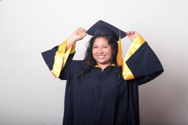 Mezuniyetini kutlamak için kep ve cübbe giyen 25 yaşında genç esmer bir kadın. Gururlu, memnun ve mutlu bir şekilde okulu bitirmiş.