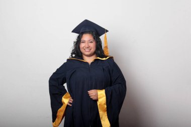 Mezuniyetini kutlamak için kep ve cübbe giyen 25 yaşında genç esmer bir kadın. Gururlu, memnun ve mutlu bir şekilde okulu bitirmiş.