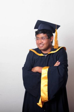 30 yaşında esmer tenli, gözlüklü bir adam mezuniyetini ve okulunu kutlamak için kep ve cüppe giyiyor.