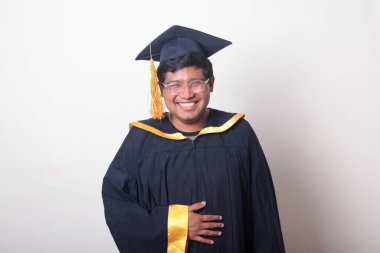 30 yaşında esmer tenli, gözlüklü bir adam mezuniyetini ve okulunu kutlamak için kep ve cüppe giyiyor.