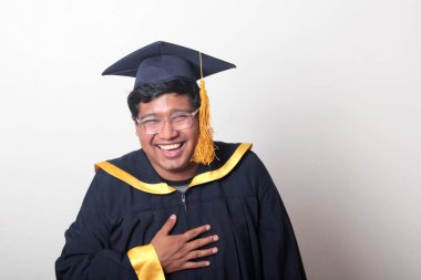 30 yaşında esmer tenli, gözlüklü bir adam mezuniyetini ve okulunu kutlamak için kep ve cüppe giyiyor.