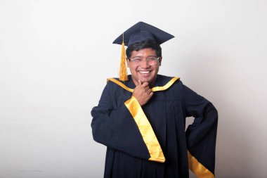 30 yaşında esmer tenli, gözlüklü bir adam mezuniyetini ve okulunu kutlamak için kep ve cüppe giyiyor.