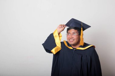 30 yaşında esmer tenli, gözlüklü bir adam mezuniyetini ve okulunu kutlamak için kep ve cüppe giyiyor.