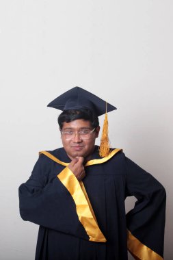 30 yaşında esmer tenli, gözlüklü bir adam mezuniyetini ve okulunu kutlamak için kep ve cüppe giyiyor.