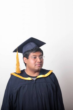 30 yaşında esmer tenli, gözlüklü bir adam mezuniyetini ve okulunu kutlamak için kep ve cüppe giyiyor.