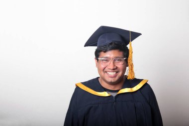 30 yaşında esmer tenli, gözlüklü bir adam mezuniyetini ve okulunu kutlamak için kep ve cüppe giyiyor.