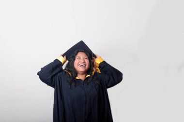 Mezuniyetini kutlamak için kep ve cübbe giyen 25 yaşında genç esmer bir kadın. Gururlu, memnun ve mutlu bir şekilde okulu bitirmiş.