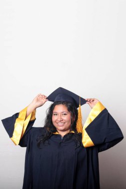 Mezuniyetini kutlamak için kep ve cübbe giyen 25 yaşında genç esmer bir kadın. Gururlu, memnun ve mutlu bir şekilde okulu bitirmiş.