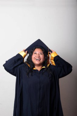 Mezuniyetini kutlamak için kep ve cübbe giyen 25 yaşında genç esmer bir kadın. Gururlu, memnun ve mutlu bir şekilde okulu bitirmiş.