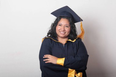 Mezuniyetini kutlamak için kep ve cübbe giyen 25 yaşında genç esmer bir kadın. Gururlu, memnun ve mutlu bir şekilde okulu bitirmiş.