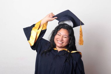 Mezuniyetini kutlamak için kep ve cübbe giyen 25 yaşında genç esmer bir kadın. Gururlu, memnun ve mutlu bir şekilde okulu bitirmiş.