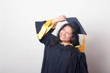 Mezuniyetini kutlamak için kep ve cübbe giyen 25 yaşında genç esmer bir kadın. Gururlu, memnun ve mutlu bir şekilde okulu bitirmiş.