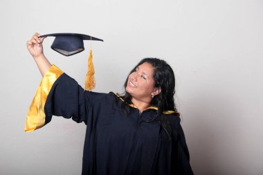 Mezuniyetini kutlamak için kep ve cübbe giyen 25 yaşında genç esmer bir kadın. Gururlu, memnun ve mutlu bir şekilde okulu bitirmiş.