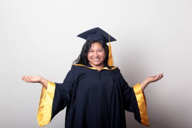 Mezuniyetini kutlamak için kep ve cübbe giyen 25 yaşında genç esmer bir kadın. Gururlu, memnun ve mutlu bir şekilde okulu bitirmiş.