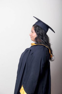 Mezuniyetini kutlamak için kep ve cübbe giyen 25 yaşında genç esmer bir kadın. Gururlu, memnun ve mutlu bir şekilde okulu bitirmiş.