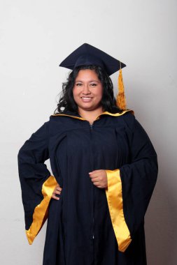 Mezuniyetini kutlamak için kep ve cübbe giyen 25 yaşında genç esmer bir kadın. Gururlu, memnun ve mutlu bir şekilde okulu bitirmiş.