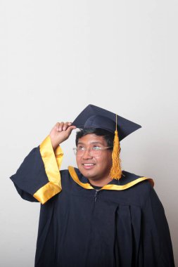 30 yaşında esmer tenli, gözlüklü bir adam mezuniyetini ve okulunu kutlamak için kep ve cüppe giyiyor.