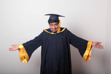 30 yaşında esmer tenli, gözlüklü bir adam mezuniyetini ve okulunu kutlamak için kep ve cüppe giyiyor.