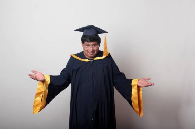 30 yaşında esmer tenli, gözlüklü bir adam mezuniyetini ve okulunu kutlamak için kep ve cüppe giyiyor.