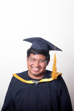 30 yaşında esmer tenli, gözlüklü bir adam mezuniyetini ve okulunu kutlamak için kep ve cüppe giyiyor.