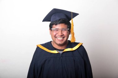 30 yaşında esmer tenli, gözlüklü bir adam mezuniyetini ve okulunu kutlamak için kep ve cüppe giyiyor.