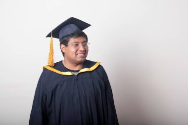 30 yaşında esmer tenli, gözlüklü bir adam mezuniyetini ve okulunu kutlamak için kep ve cüppe giyiyor.