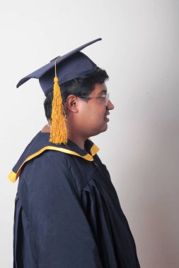 30 yaşında esmer tenli, gözlüklü bir adam mezuniyetini ve okulunu kutlamak için kep ve cüppe giyiyor.