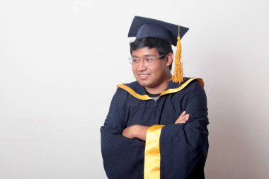 30 yaşında esmer tenli, gözlüklü bir adam mezuniyetini ve okulunu kutlamak için kep ve cüppe giyiyor.