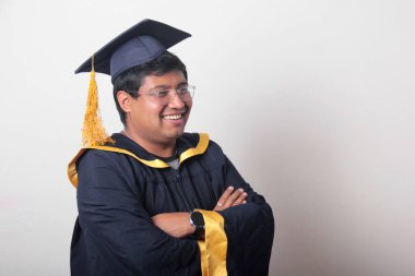 30 yaşında esmer tenli, gözlüklü bir adam mezuniyetini ve okulunu kutlamak için kep ve cüppe giyiyor.