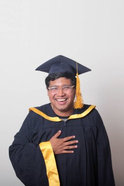 30 yaşında esmer tenli, gözlüklü bir adam mezuniyetini ve okulunu kutlamak için kep ve cüppe giyiyor.