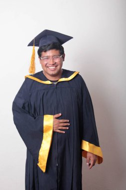 30 yaşında esmer tenli, gözlüklü bir adam mezuniyetini ve okulunu kutlamak için kep ve cüppe giyiyor.