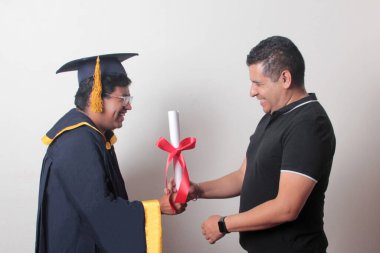 Gururlu ve memnun bir bekar baba, kep ve cübbe giymiş esmer Latin oğlu ile okulun sonunu kutluyor.