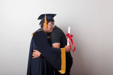 Gururlu ve memnun bir bekar baba, kep ve cübbe giymiş esmer Latin oğlu ile okulun sonunu kutluyor.