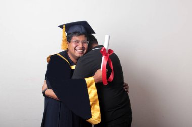 Gururlu ve memnun bir bekar baba, kep ve cübbe giymiş esmer Latin oğlu ile okulun sonunu kutluyor.