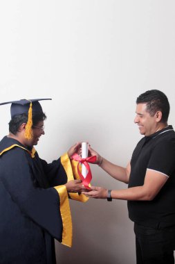 Gururlu ve memnun bir bekar baba, kep ve cübbe giymiş esmer Latin oğlu ile okulun sonunu kutluyor.