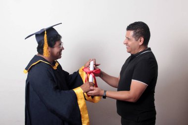 Gururlu ve memnun bir bekar baba, kep ve cübbe giymiş esmer Latin oğlu ile okulun sonunu kutluyor.