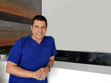 Mavi cerrahi önlük giyen koyu tenli Latin bir erkek doktor hastanede çalışıyor ve başarılı, üretken ve çalışkan görünüyor.