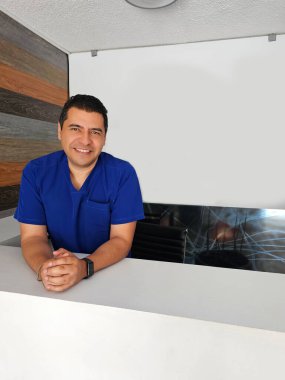 Mavi cerrahi önlük giyen koyu tenli Latin bir erkek doktor hastanede çalışıyor ve başarılı, üretken ve çalışkan görünüyor.