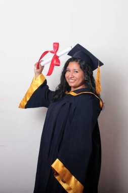 Şapka ve cübbe giymiş genç esmer kadın diplomasını gururla, tatmin olmuş ve kariyerini okulunda bitirmekten mutlu olarak gösteriyor.