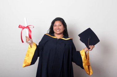 Şapka ve cübbe giymiş genç esmer kadın diplomasını gururla, tatmin olmuş ve kariyerini okulunda bitirmekten mutlu olarak gösteriyor.