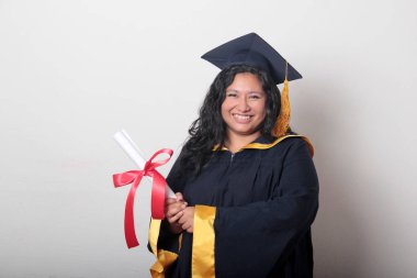 Şapka ve cübbe giymiş genç esmer kadın diplomasını gururla, tatmin olmuş ve kariyerini okulunda bitirmekten mutlu olarak gösteriyor.