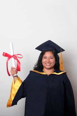 Şapka ve cübbe giymiş genç esmer kadın diplomasını gururla, tatmin olmuş ve kariyerini okulunda bitirmekten mutlu olarak gösteriyor.